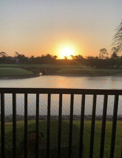 Sunset over a calm lake viewed from a balcony with railing in the foreground.