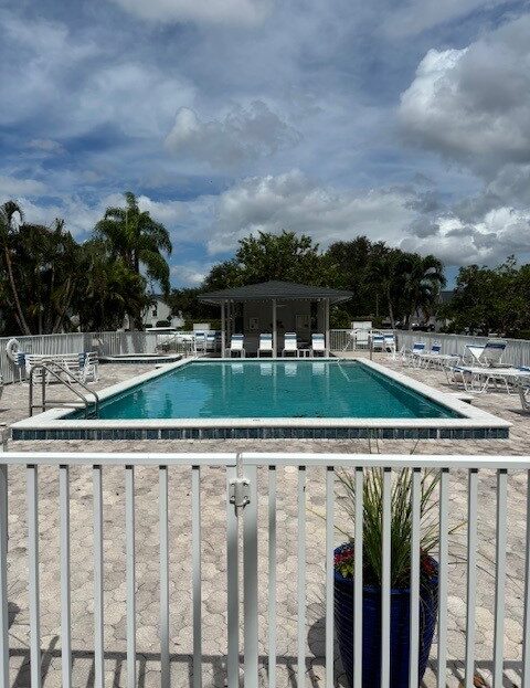 Empty outdoor pool with lounge chairs under a cloudy sky.