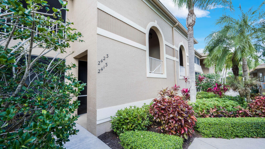 Well-maintained garden and walkway alongside a beige stucco house with arched windows.