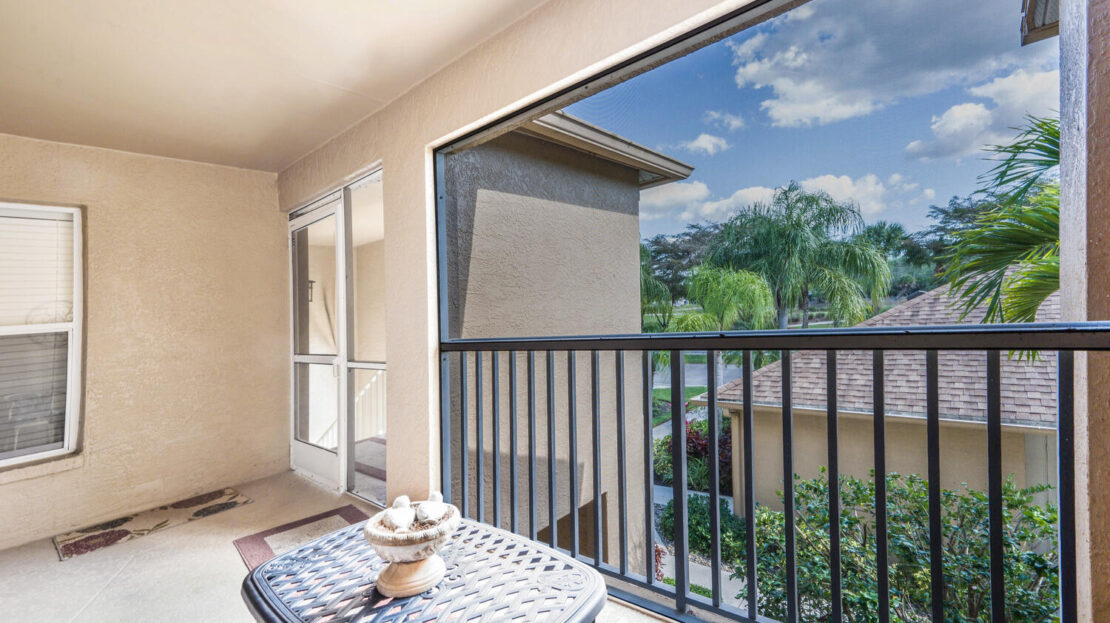 Balcony with a small table and decorative piece overlooking greenery and a sunny sky.