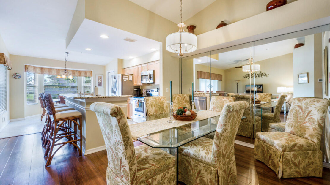 Elegant dining area with glass table and patterned chairs under a chandelier.