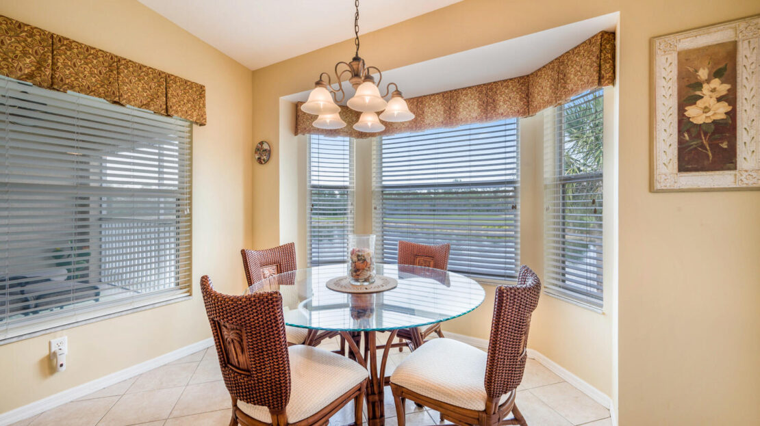 Cozy breakfast nook with glass table and bay windows overlooking a serene lake.