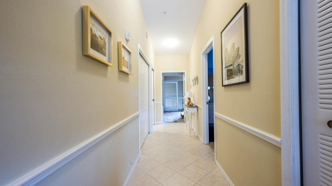 Bright hallway with framed artwork and beige walls leading to a living area.