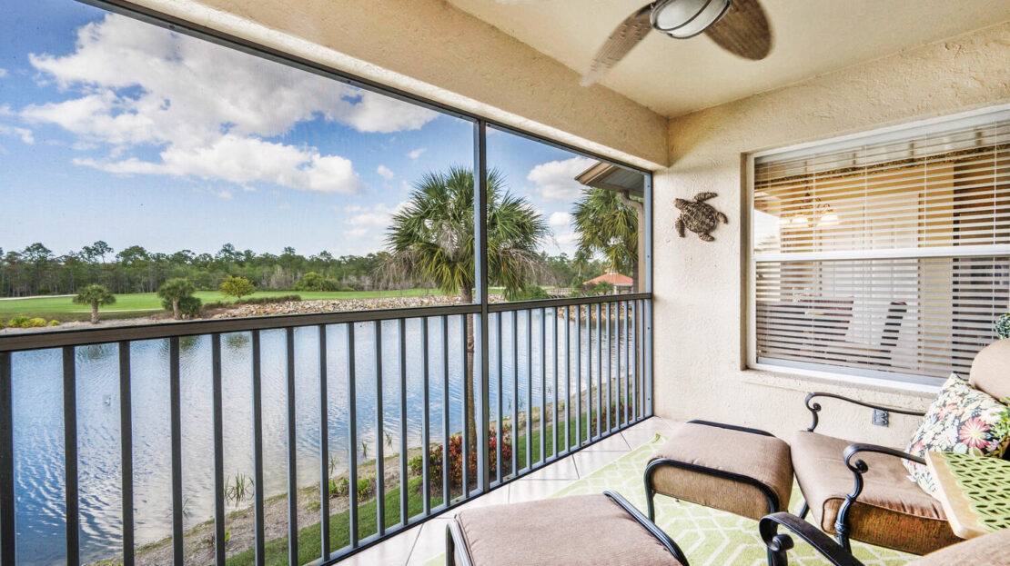 Cozy balcony overlooking a serene lake with comfortable seating and ceiling fan.