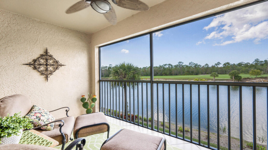 Balcony with cushioned chairs overlooking a tranquil lake.