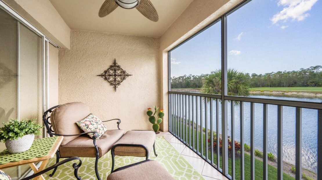 Cozy balcony with seating overlooking a serene lake and lush greenery.