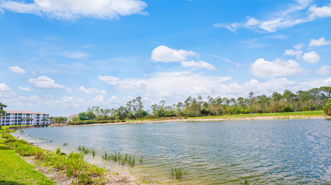Calm river flowing beside a grassy bank under a blue sky.