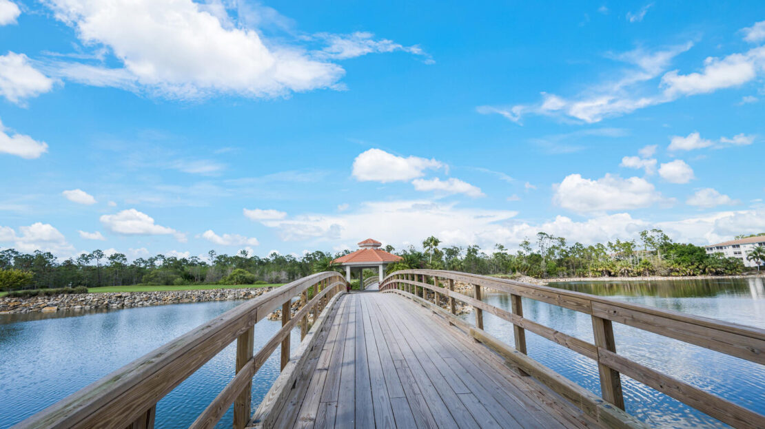 Wooden boardwalk leading to a gazebo over water under a blue sky.
