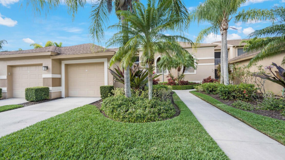 A well-maintained residential street with palm trees and green lawns under a blue sky.