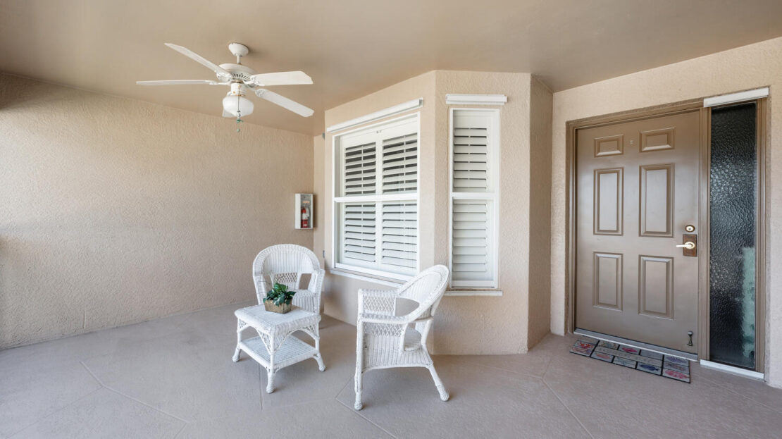 Cozy porch with white wicker chairs and a ceiling fan.