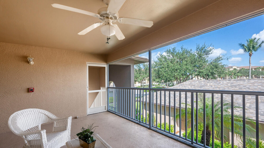 Cozy balcony with ceiling fan overlooking greenery and rooftops.