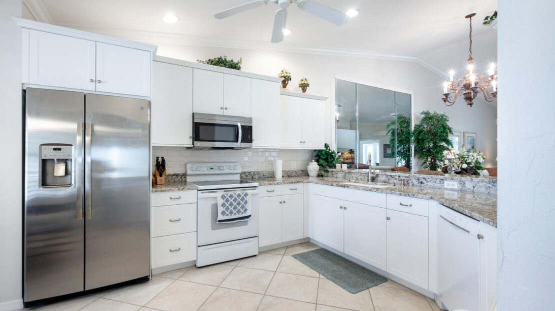 Bright, modern white kitchen with stainless steel appliances and green plants.