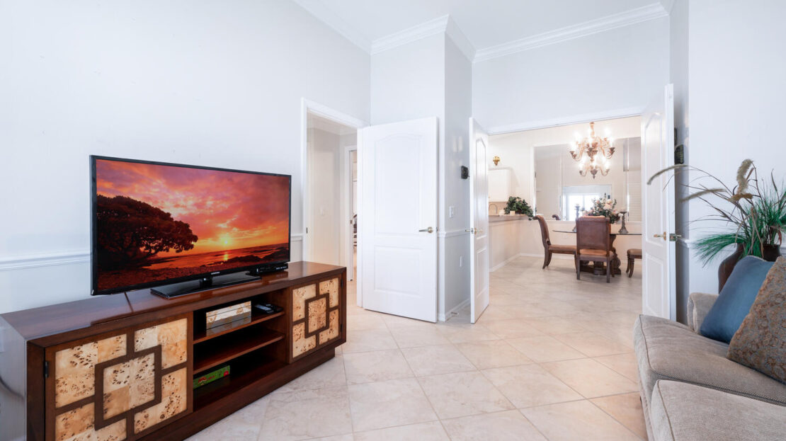 Bright living room with TV on wooden stand and view into dining area.