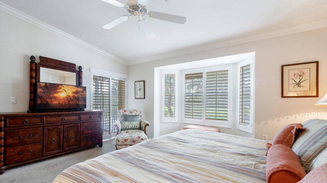 Bright bedroom with a large window, ceiling fan, and TV on a wooden dresser.
