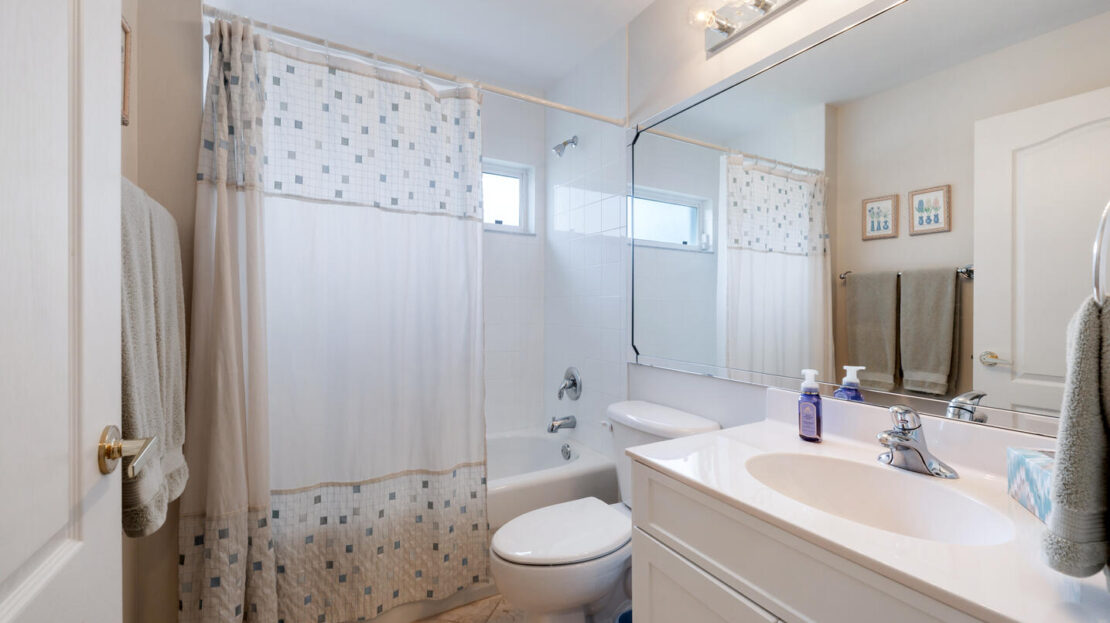 Bright bathroom with white vanity, toilet, and a shower with a patterned curtain.