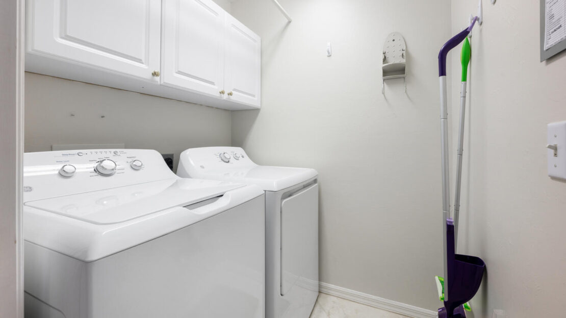 A clean laundry room with washer, dryer, and storage cabinets.