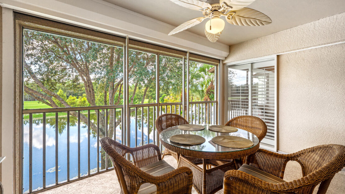 Cozy screened patio with wicker furniture overlooking a serene lake.