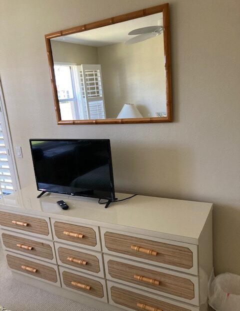 A TV sits on a white dresser beneath a large wall mirror.