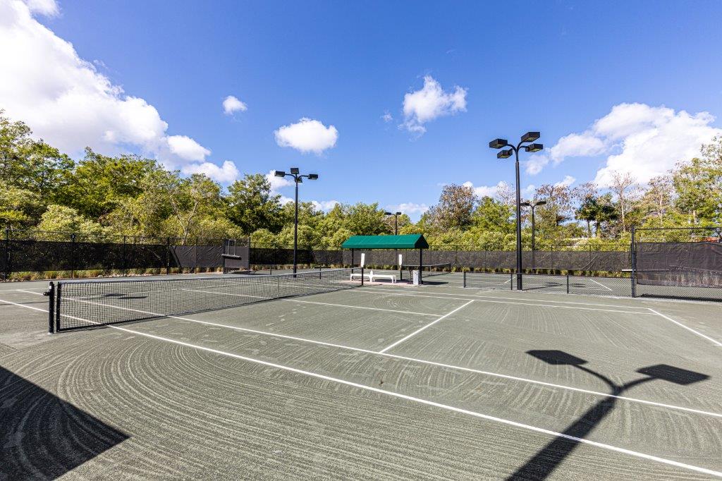 An empty outdoor tennis court under a sunny sky.
