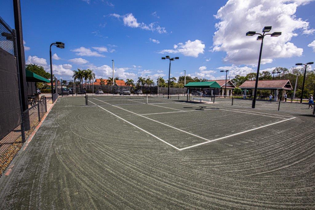 Empty outdoor tennis court under a partly cloudy sky.