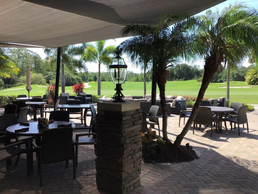 Outdoor seating area with tables, chairs, and palm trees overlooking a golf course.
