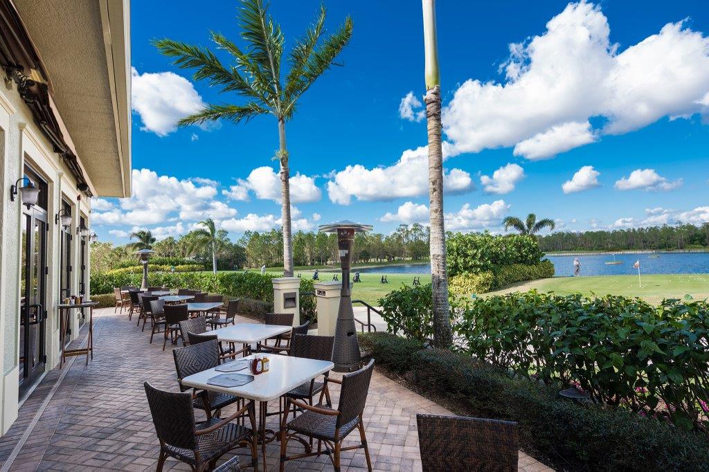 Outdoor dining area with tables, chairs, and palm trees under a blue sky.