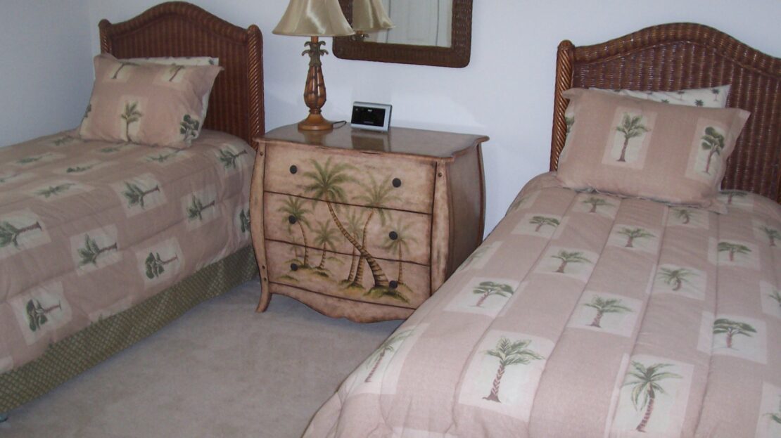 Two twin beds with matching floral bedspreads and a vintage nightstand between them.