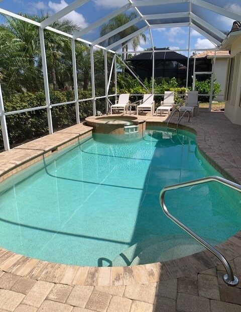 A backyard pool with clear water and lounge chairs in a screened enclosure.