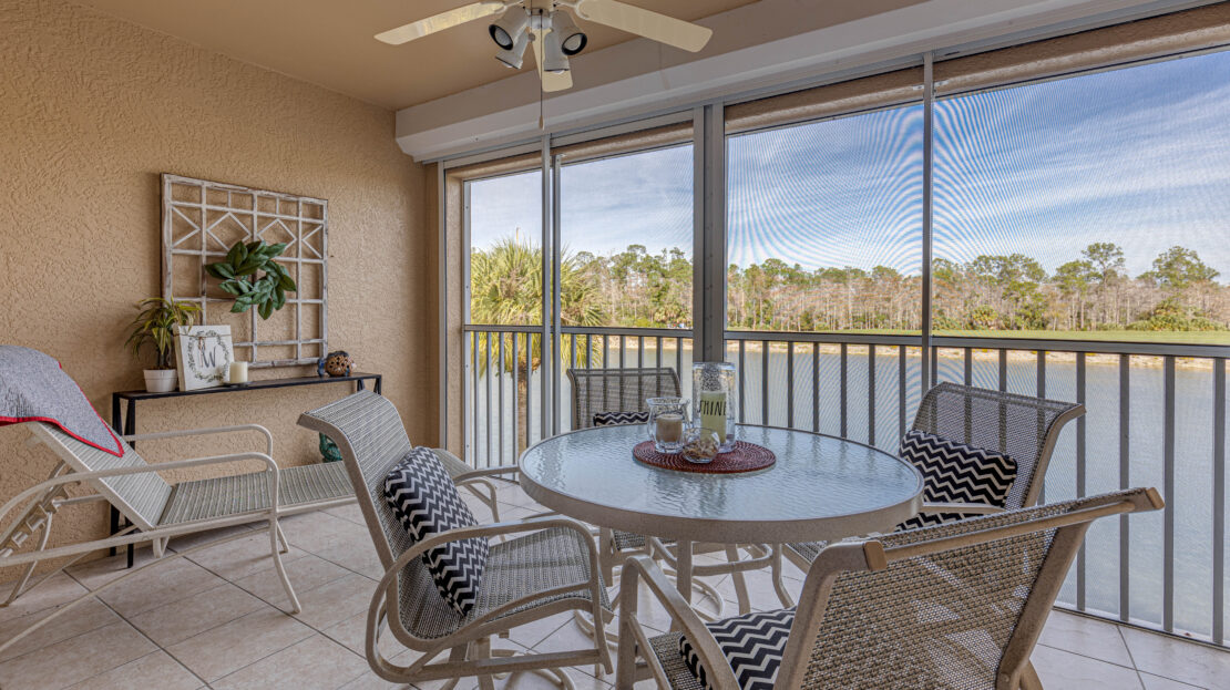 Cozy screened porch with wicker furniture and scenic lake view.