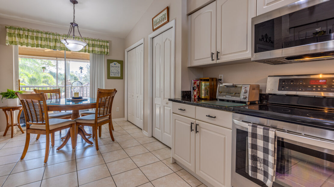 Bright kitchen with white cabinets, tiled floor, and a round dining table by a sliding glass door.