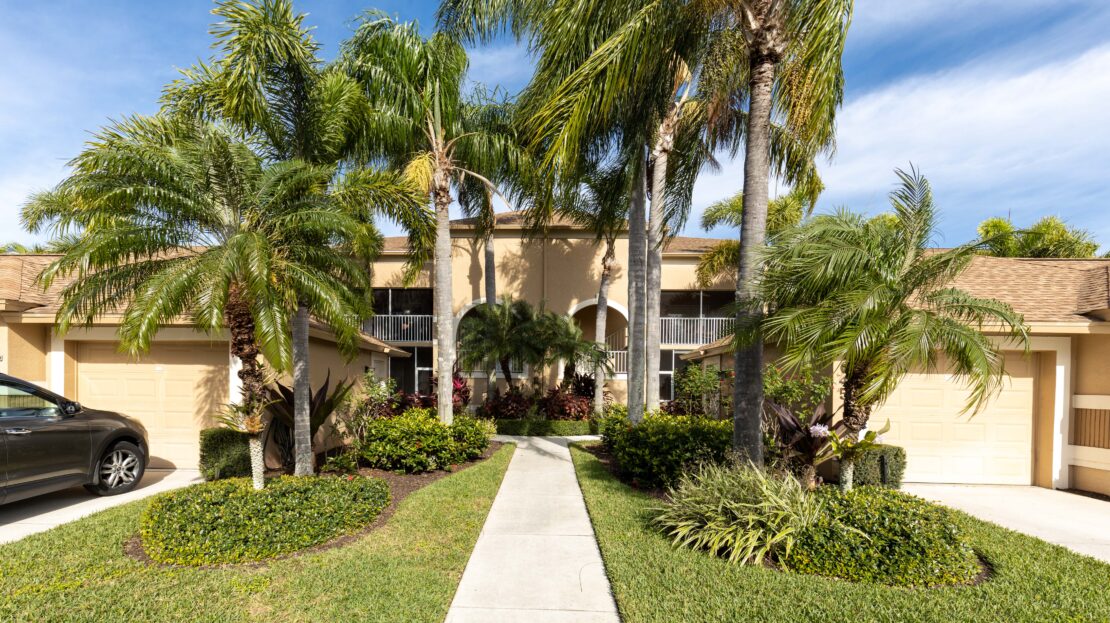 Pathway leading to a beige residential building surrounded by palm trees and greenery.