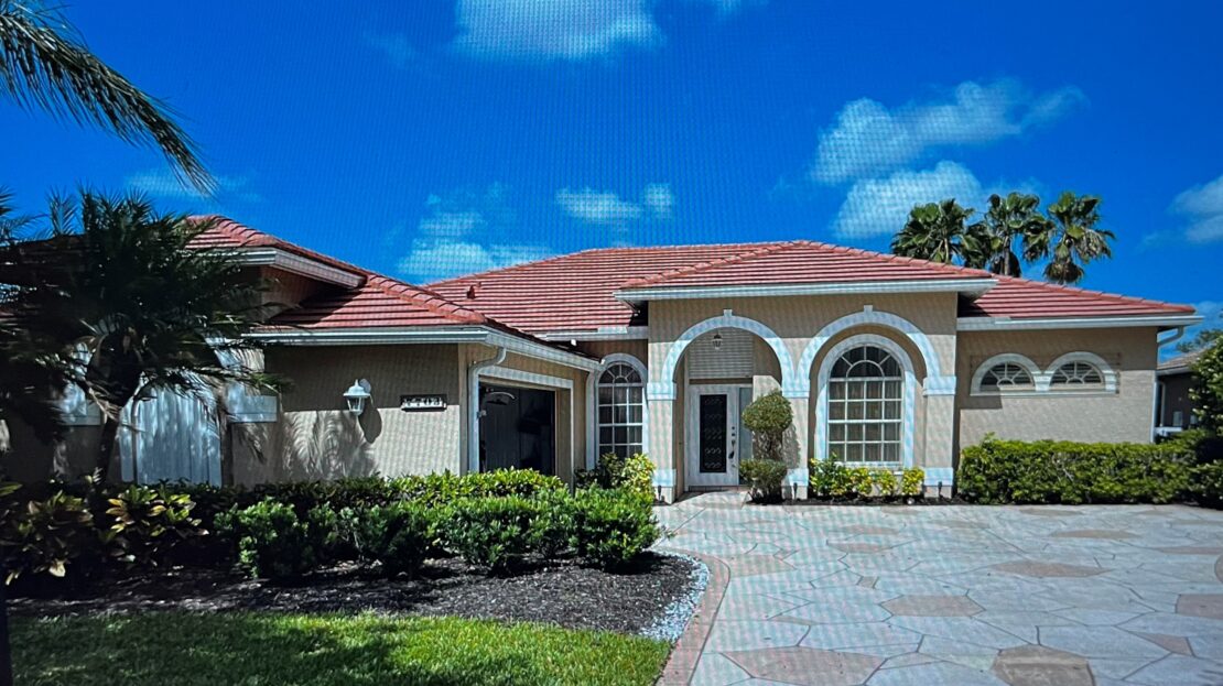 A large beige house with red roof tiles and arched windows under a blue sky.