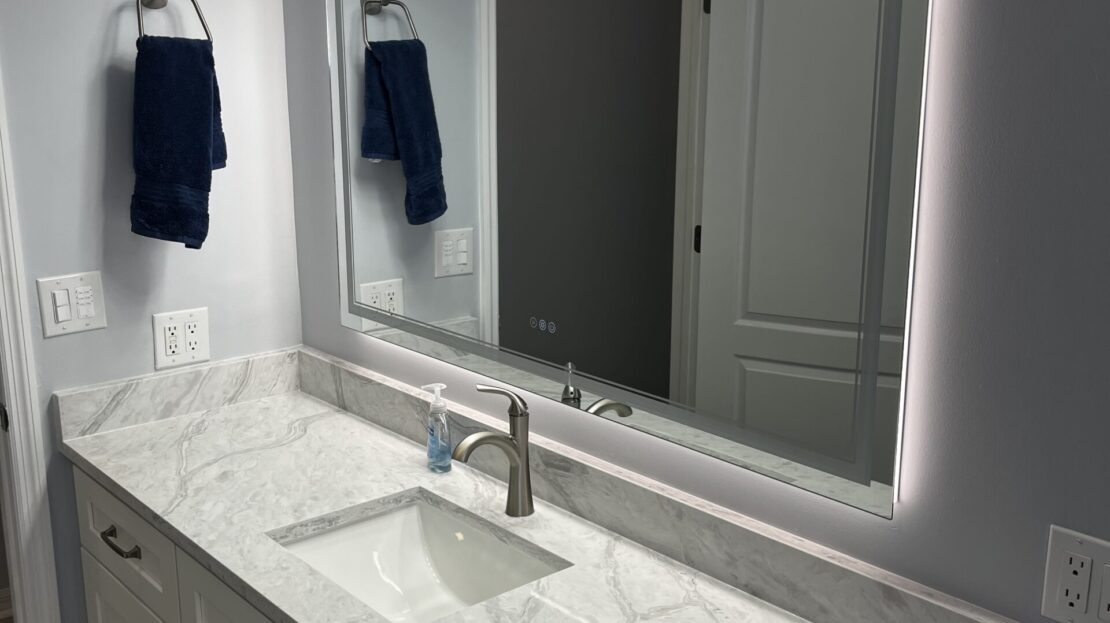 Modern bathroom vanity with marble countertop and illuminated mirror.