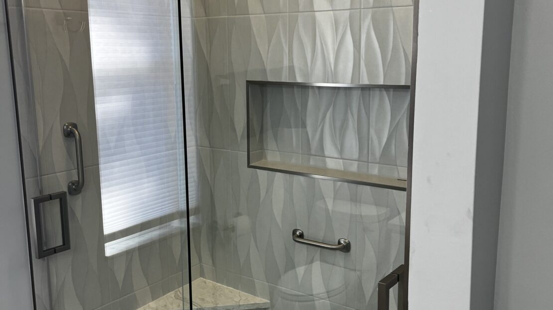 Modern bathroom with glass shower and marble wall tiles.
