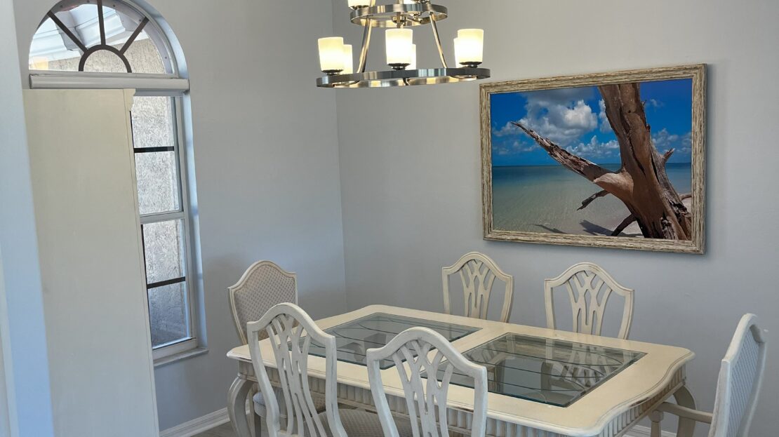 Elegant dining room with white furniture and coastal artwork.