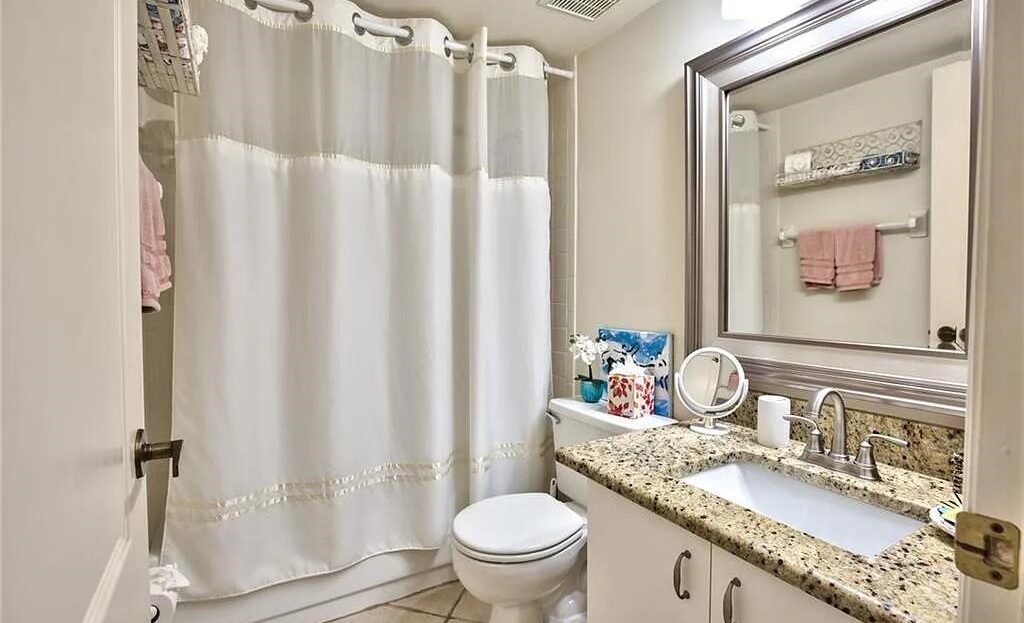 Bright bathroom with white shower curtain and granite countertop.