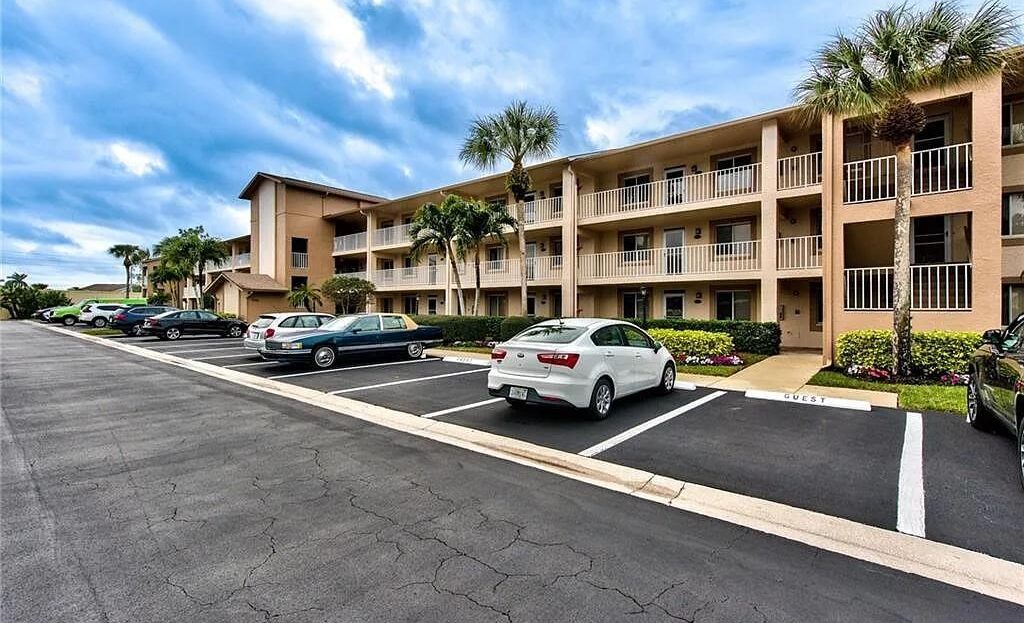 Apartment building with parked cars under a blue sky.