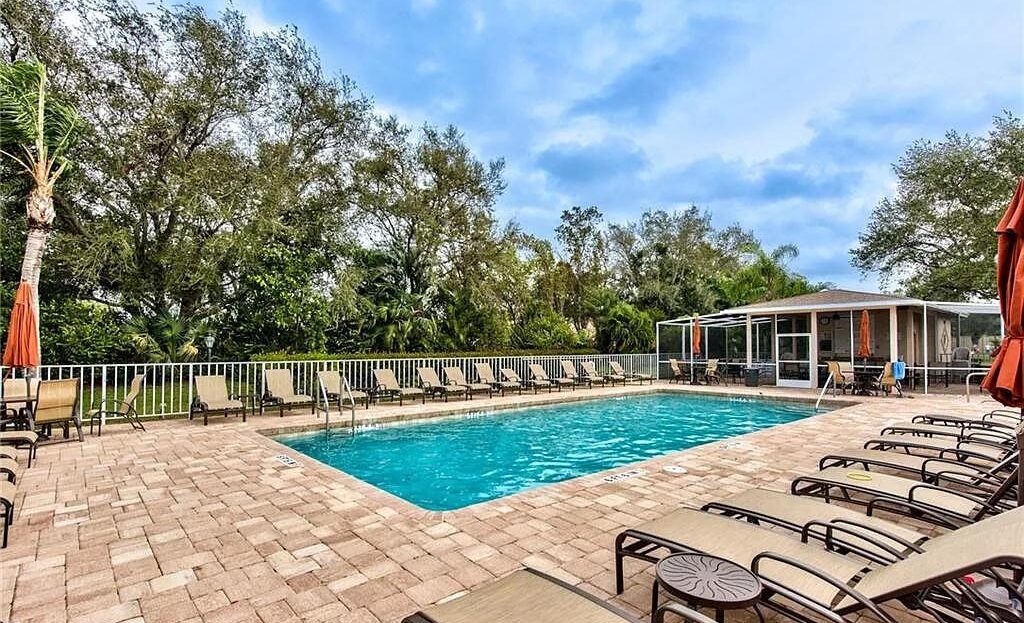 Outdoor swimming pool with lounge chairs under a partly cloudy sky.