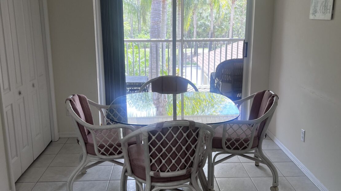 Bright dining area with glass table and four cushioned chairs.
