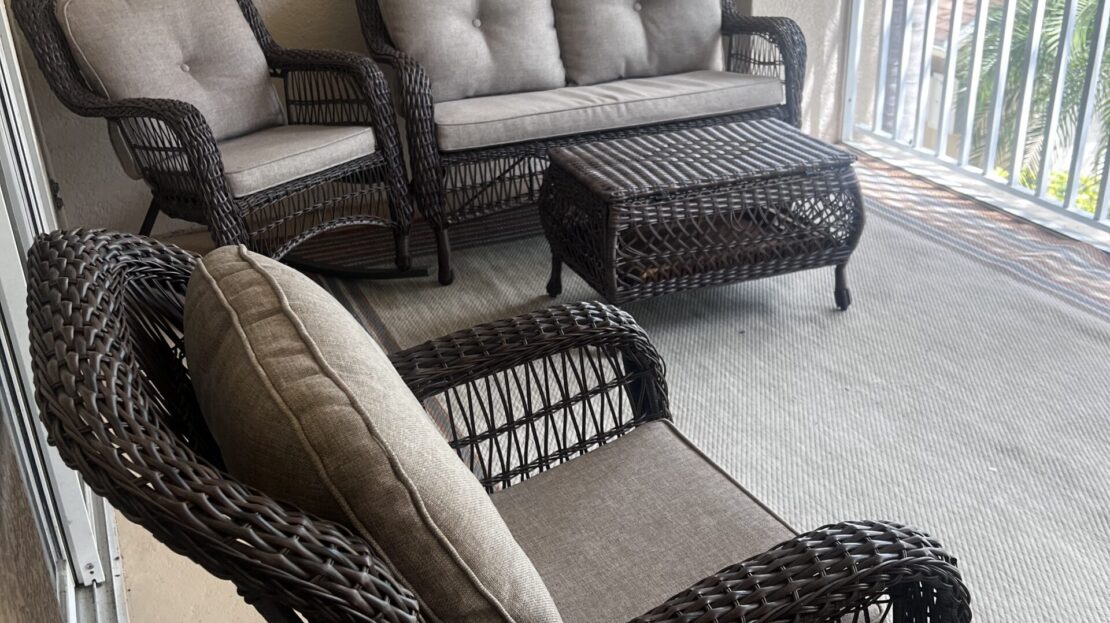 Wicker patio furniture set on a balcony with cushions and a view.