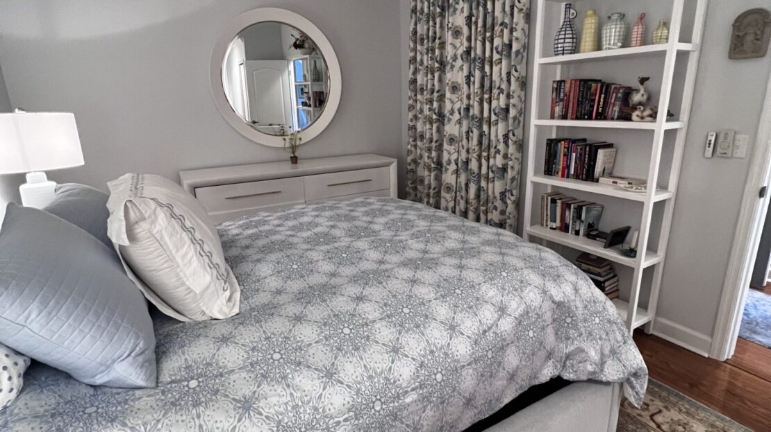 Cozy bedroom with patterned bedding and a large round mirror on the wall.