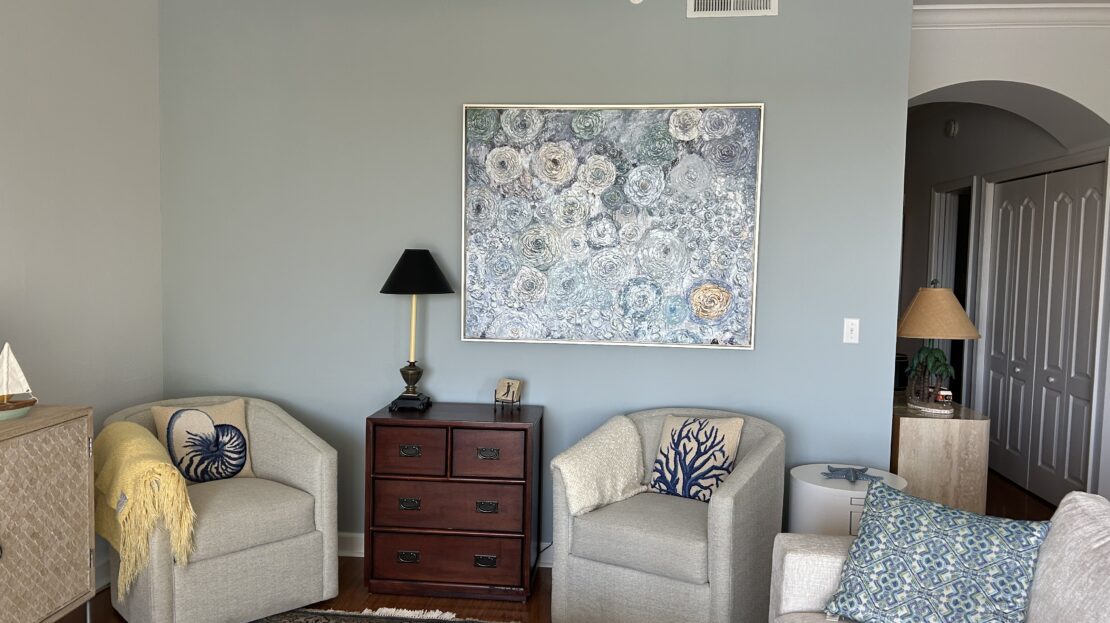 Cozy living room with beige chairs and floral artwork on gray wall.
