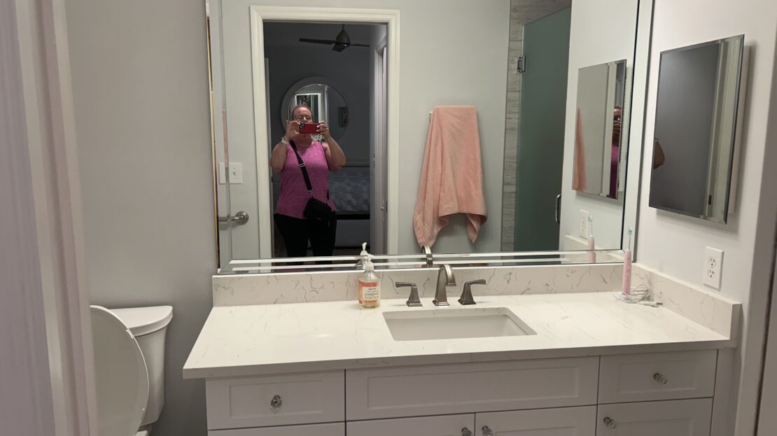 A modern bathroom vanity with a large mirror and white cabinets.