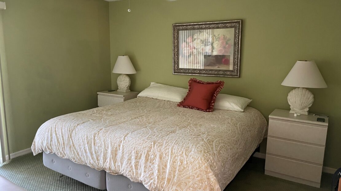 Cozy bedroom with green walls and neutral bedding accented by a red pillow.