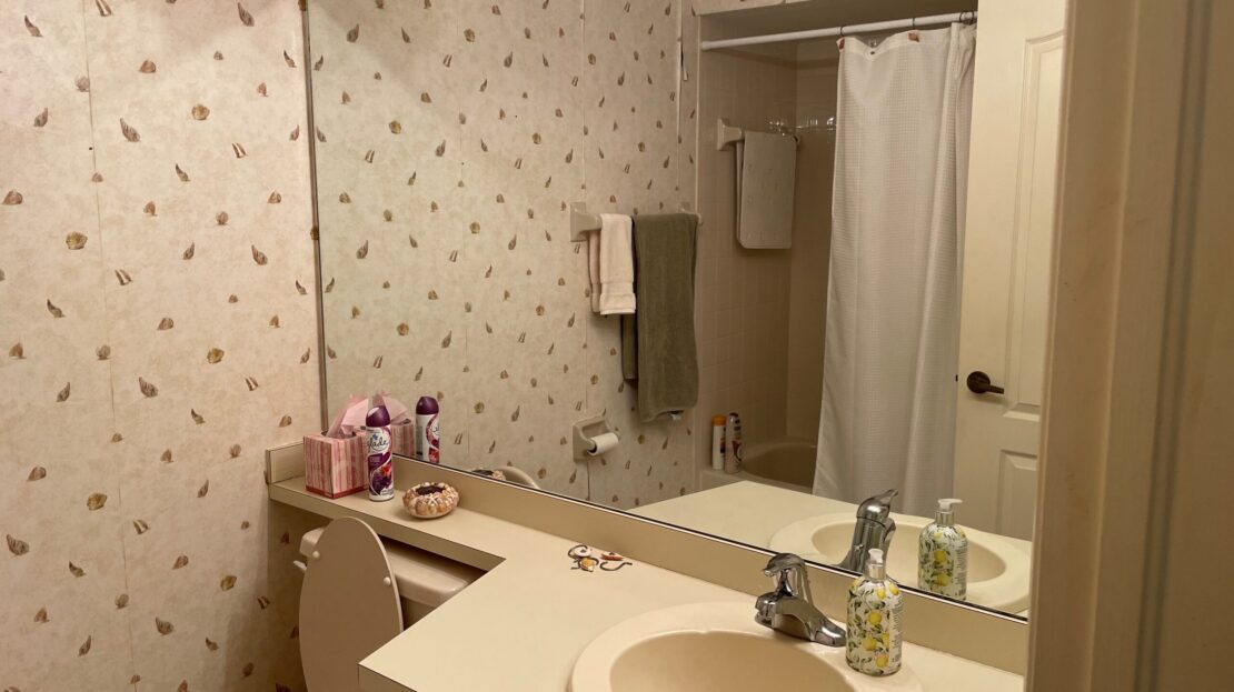 Cozy bathroom with floral wallpaper and a large mirror above the sink.