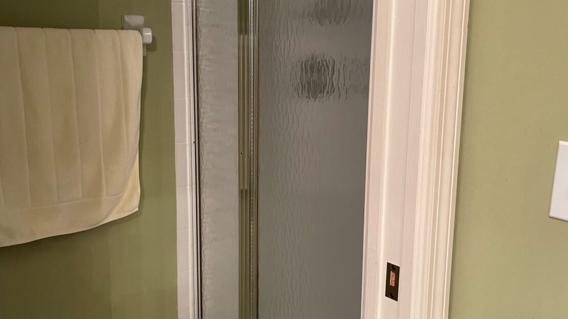 Compact corner shower with glass door in a bathroom with green walls.