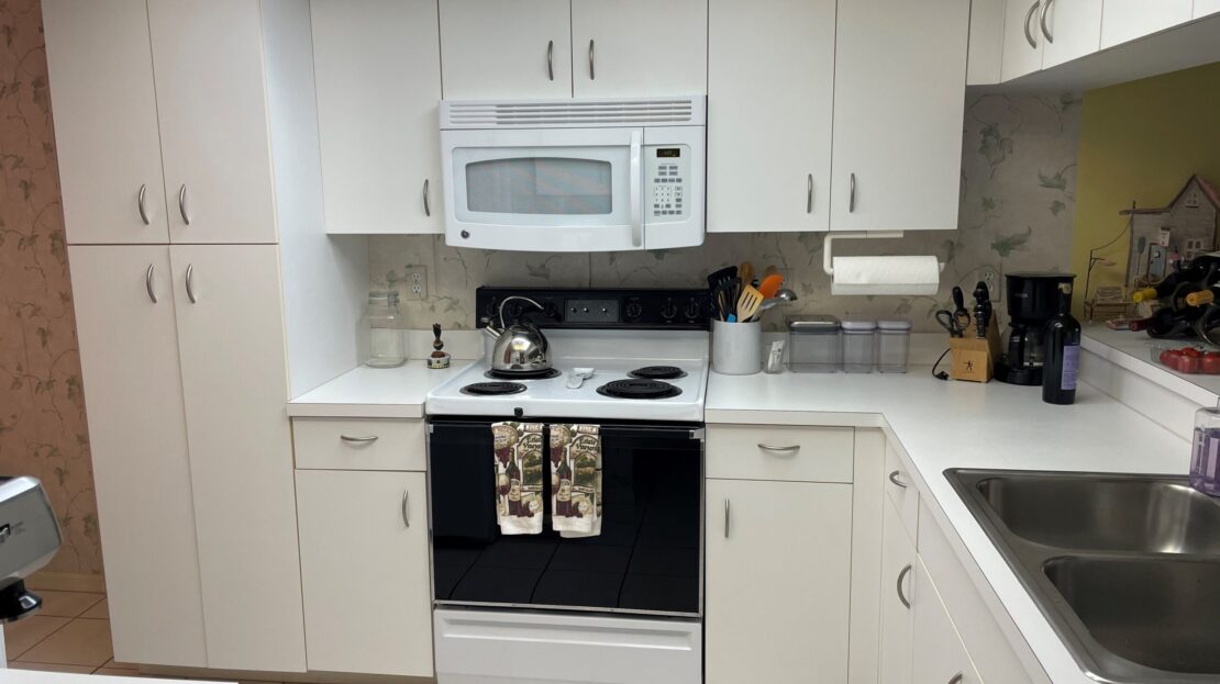 Modern white kitchen with black stove and microwave.