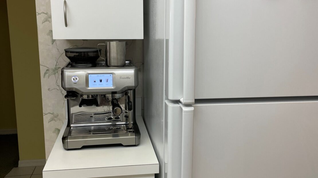 Espresso machine and fridge in a kitchen corner.