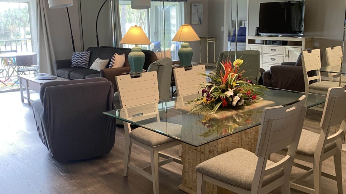 Modern dining area with glass table and cozy living space in the background.