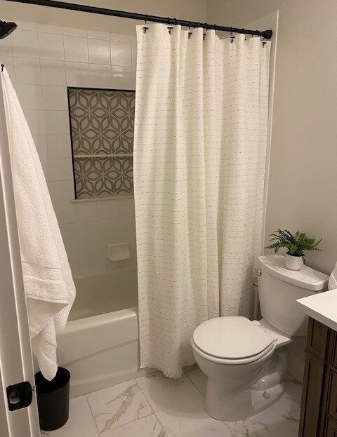 Clean bathroom with white towels, a shower curtain, and a small plant on the toilet tank.